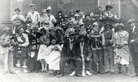 Photograph showing thirty three men in Fancy Dress grouped outside a building which may be the school at Blackhall; the men are dressed as pierrots, soldiers, Charlie Chaplin,women, and Black and White Minstrels and a number are holding musical instruments; they have been identified as being in Blackhall