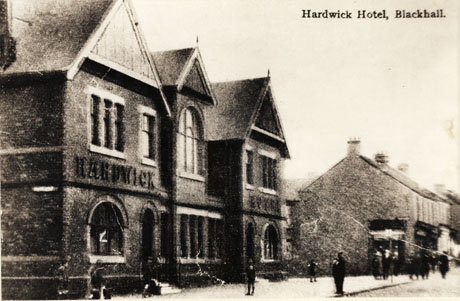 Postcard photograph, entitled Hardwick Hotel, Blackhall, showing the exterior of the hotel fronting on to the street: the name of the hotel can be seen on the wall of the hotel; and a block of shops beyond the hotel, and indistinct figures on the pavement near the hotel and shops can also be seen
