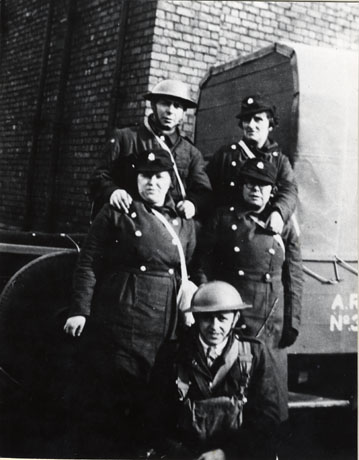 Photograph of two men and three women, described as members of the Air Raid Precautions organisation during the Second World War; they are all in uniform, with the women wearing greatcoats and soft hats and the men overalls and steel helmets; they are posed outside a building described as The Granary; a part of a lorry, with A.R.P. No 3... written on it, can also be seen.