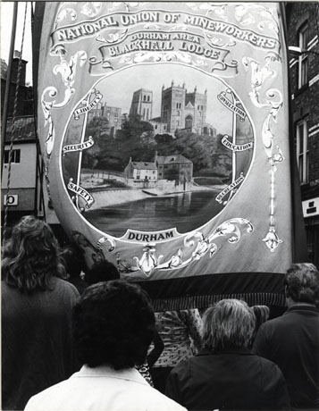 Photograph showing the banner of Blackhall Lodge being carried at the Miners' Gala in North Road, Durham City; the banner shows a picture of Durham Cathedral, with the Fulling Mill and the River Wear in the foreground; the backs of the heads of those carrying the banner only can be seen.