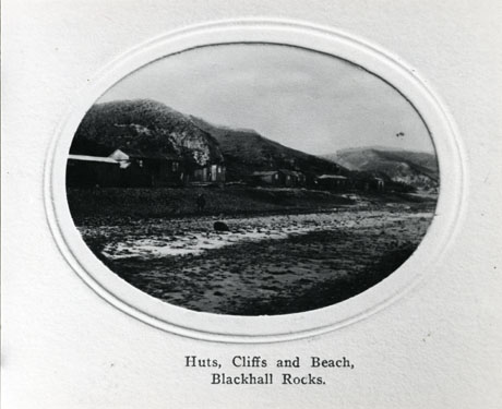 Postcard, or illustration from a volume, entitled Huts, Cliffs and Beach, Blackhall Rocks, showing the beach with the cliffs in the distance, and, below the cliffs, a number of huts; the image is fairly indistinct and the number and appearance of the huts cannot be determined with accuracy.