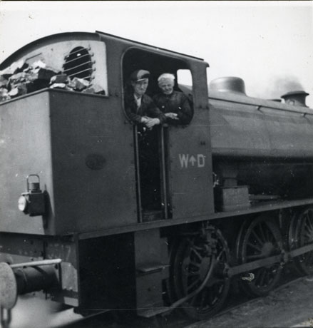 Photograph, described as Blackhall Locomotive, of a steam locomotive, photographed from the side, showing the side of the footplate bearing the letters W D and showing two men looking out from the footplate, identified as Bob Dunn and Chris Keen; only part of the rest of the locomotive may be seen