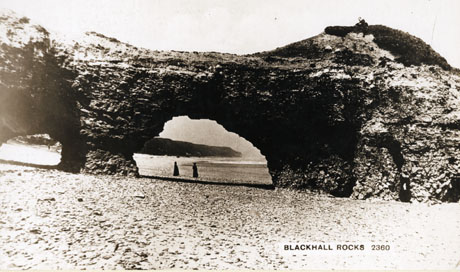 Postcard photograph entitled Blackhall Rocks 2360 showing rocks jutting into the sea with caves in them, through which may be seen two indistinct female figures in the dress of the early years of the twentieth century
