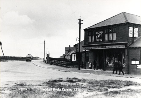 Postcard photograph entitled Blackhall Rocks Corner and described as View showing coast road, Blackhall showing the same view from, a slightly different angle, as blac0085, including I. Pieroni's grocery and confectionery shop, which in this photograph, also advertises itself as Blackhall Rocks Cafe; the view along the road is more extensive with an indistinct lorry in the middle distance; two indistinct men, and a woman with a pushchair may be seen in front of Pieroni's shop