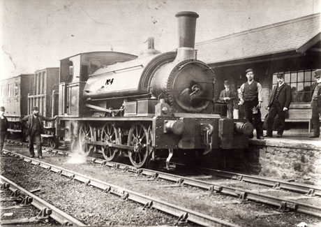 Photograph showing a locomotive bearing the number four, facing the camera, standing in a railway station, presumably at Blackhall Rocks; the locomotive is pulling passenger carriages; two men are standing beside the locomotive on the tracks; a man with an oil can is standing near the locomotive on the platform, along with an employee in railway uniform and two men in suits