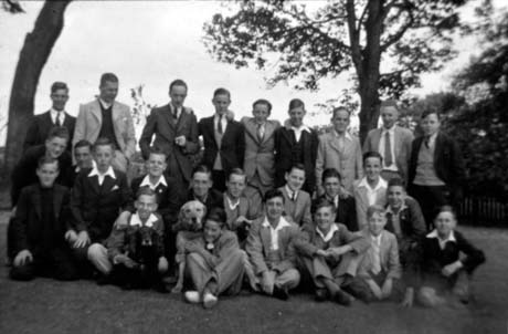 Photograph of twenty three young men and boys, aged between approximately thirteen and twenty years, posed under two trees; they are all wearing jackets and trousers; two of the young men have dogs; they have been identified as Blackhall Boys' Club