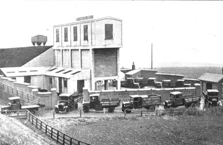 Photograph showing a colliery building with lorries driving round it and out of its yard; the lorries have the words The Horden Collieries Ltd. Blackhall Colliery on them; a coal waggon can be seen on the horizon behind the building; the photograph shows the same scene as blac103