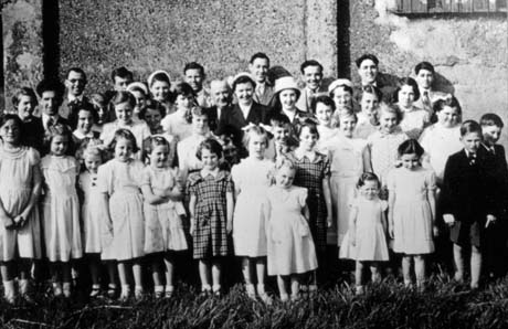 Photograph of approximately thirty children, aged between four and fourteen years, wearing summer dresses and suits, posed against a wall, with eight men and three women; they have been described as members of the Blackhall Wesleyan Methodist Church Sunday School