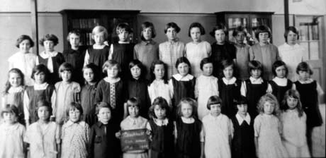 Photograph of thirty six girls, aged approximately ten years, posed in a classroom with cupboards behind the girls; a girl on the front row is carrying a notice which appears to read: Blackhall Girls' School, but the photograph has been identified as the Roman Catholic School at Blackhall
