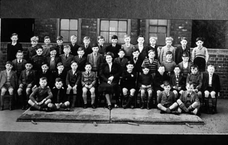 Photograph of thirty eight boys, aged approximately seven years, posed outside a building with a middle-aged woman sitting in the middle of the front row; they have been identified as pupils at Blackhall Junior School