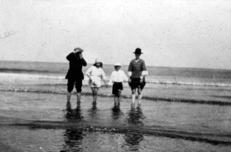 Photograph of the indistinct figures of a man, a woman and two children aged approximately nine and seven years, standing in the shallows of the sea with the open sea behind them;