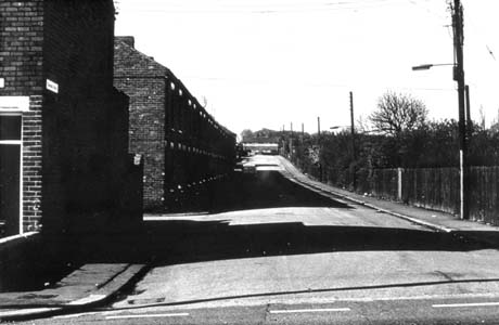 Photograph showing a narrow road with terraced houses on the left and a hedge on the right, running away from the camera; the photograph is dark and somewhat indistinct; it has been identified as East Street, Blackhall