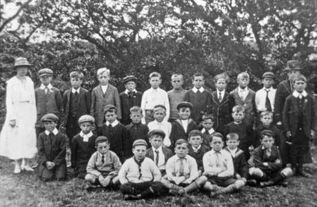 Photograph of twenty six boys aged approximately nine years posed under trees with two women, who are dressed in hats and dresses; the boys are dressed in caps, ties and jackets; the group has been identified as Blackhall Church Outing