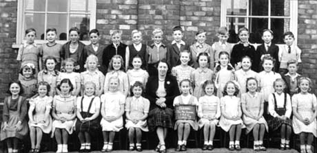 Photograph of thirty six children aged approximately seven years posed against the wall of a brick building; a woman is sitting in the middle of the front row; a child is holding a notice reading as follows: Blackwell Junior Mixed School 1950 Class 3