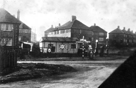 Photograph showing the surface of a road in the foreground with another road at right angles to it; beyond the second road is a finger post with signs pointing in four directions; beyond the finger post are semi-detached houses and a garage; the picture has been identified as Blackhall Four Lane Ends