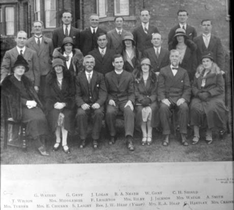 Photograph showing thirteen men and seven women, possibly members of the Parochial Church Council, posed in front of the exterior of a house; they are wearing suits and overcoats; they have been identified as follows: Back Row, Left to Right: G. Waters; G. Gent; J. Logan; R. A. Neath; W. Gent; C. H. Shield; Middle Row, Left to Right: T. Wilson; Mrs. Middlemiss; F. Leighton; Mrs. Riley; J. Jackson; Mrs. Waugh; A. Smith; Front Row, Left to Right: Mrs. Turner; Mrs. E. Chicken; S. Laight; Rev. J. W. Heap(Vicar); Mrs. E. A. Heap; G. Hartley; Mrs. Craine