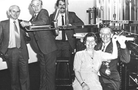 Photograph showing three men at the back of the picture dressed in suits and ties pulling part of an apparatus attached to a large metal grille; at the front of the photograph are a woman in a dress and a man in a suit and chain of office also pulling part of the apparatus; the man with the chain of office has been identified as Councillor Moses Kirkup of Blackhall