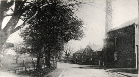 Photograph of the exterior of Castle Eden Brewery on the right of the picture, the road past the brewery in the middle of the picture; and trees and distant cottages on the left of the picture; a faint image of a wheeled vehicle can be seen in the distance