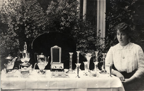 Photograph of a daughter of Colonel Burdon of Castle Eden, taken possibly in a conservatory, standing beside a table on which are displayed the presents she has received for her twenty-first birthday; Miss Burdon and her presents may be seen clearly