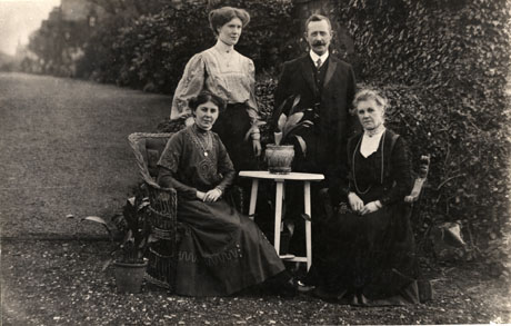 Photograph of the family Mr. Lamb, the Station Master at Castle Eden, showing a middle-aged man standing behind a small table on which a plant in a pot is standing; at his right also standing is a young woman, presumably one of his daughters; on either side of the table are sitting a middle-aged woman and a young woman, presumably his wife and daughter; the photograph is taken outdoors in a garden
