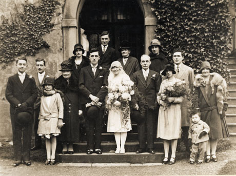Photograph of a wedding group on the steps of a church at Castle Eden, showing the bride and groom, a bridesmaid, five men, five women, and two children, one approximately twelve years old and the other approximately three years old