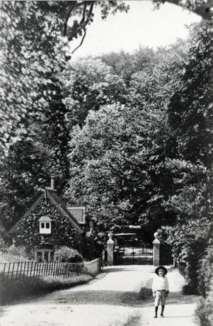 Photograph of The Lodge, Castle Eden, taken from the same direction as cast0040, cast0046, cast0066, cast0067, but from a longer distance; the gates to the park are closed and a small boy is standing in the road; the trees on the right-hand of the photograph appear to be larger than in the other photographs
