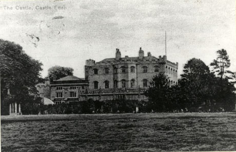 Postcard photograph entitled The Castle, Castle Eden showing the exterior of the castle from a distance across the grounds of the castle; the front and side of the castle may be seen