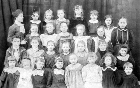 Photograph showing twenty six girls and one boy aged approximately seven years posed with a woman identified as Mrs. Stirk; the photograph has been identified as having been taken at Castle Eden