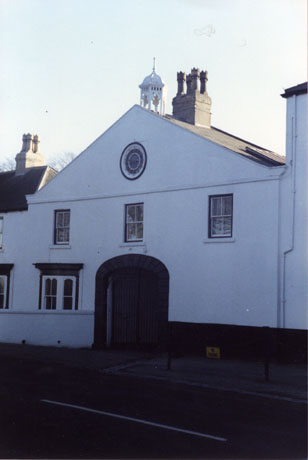 Photograph of the exterior of a white-washed building with a steep gable, a bay window and an archway on the ground floor; three sash windows on the first floor and a bellcote on the roof; the building has been identified as being in Castle Eden