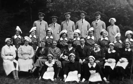 Photograph showing six men in uniform and with peaked caps standing in a row at the back of a group; next to them is a woman in an overall and cap; in front of the men are nine women in uniform and cooks' caps with ERD marked on their uniforms; on the next row, are two women in overalls and cooks' caps and four women and one man in ordinary clothes; next to them, are two women in waitresses' uniforms; on the front row are three women in waitresses' uniforms; they have been identified as Staff at Crimdon Dene