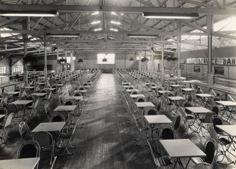 Photograph looking the length of a room with rows of tables and chairs; the Self Service Bar can be seen on the right of the photograph, which is looking the same way as 21 and 22; the building has been identified as The Pavilion, Crimdon Park, at its opening; the photograph was taken by T. G. Reeves, 351 London Road, Mitcham, Surrey