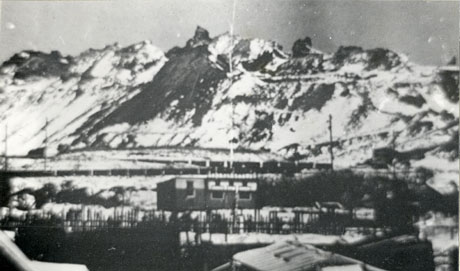 Photograph of the pit heap at Deaf Hill under snow with pigeon crees in the middle distance; the photograph is slightly blurred and little detail can be seen