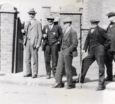 Photograph of Ramsey McDonald, with four other men, at Deaf Hill during an election; all five men are standing on the pavement of a road with a gate and wall behind them