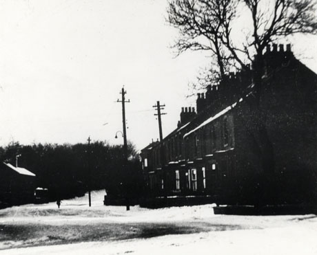 Photograph showing, on the right, a row of terraced houses with bay windows and, on the left, a very indistinct building, all under snow; the photograph is described as Deaf Hill Terrace and Comrades' Club