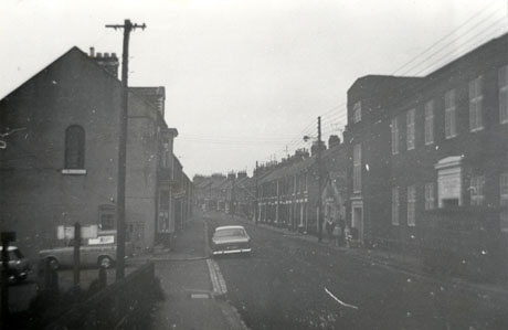 Photograph of Station Lane showing a street of terraced houses, taken from a similar viewpoint to that in deaf0016, and showing a large building on the right hand side of the street, erected since deaf0016 was taken; two cars can be seen parked in the road