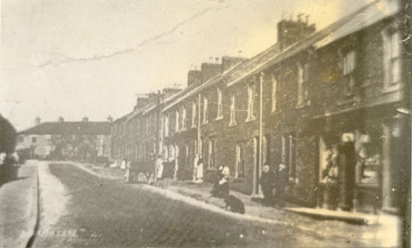 Postcard photograph entitled Station Lane, showing Top Half of Station Road, Deaf Hill; one side only of a street of terraced houses is shown, with houses beyond it in the distance;figures can be seen on the pavement