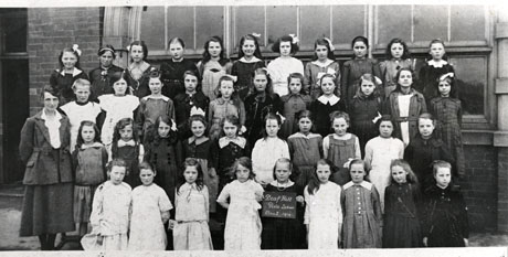 Photograph of the forty-one members of Class Two at Deaf Hill Girls' School, posed outside a brick- built building with a large window; the pupils are accompanied by their teacher