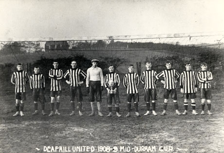 Postcard photograph entitled Deaf Hill United 1908-09 Mid Durham Cup, showing the members of the team lined up on a ground with a football net behind them and, behind that, a hill with a house on its summit; a member of the team is holding the cup