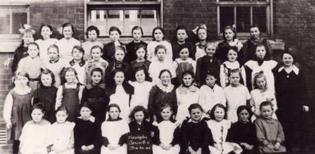 Photograph of forty three girls posed outside a building with their teacher; a girl on the front row is holding a notice reading Easington Senior Girls December(?) 1919