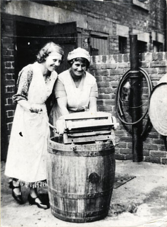 Photograph showing two women, identified as Mrs. Vickers and daughter, in the backyard of a house in Moncrief Terrace, Easington Colliery,with a dolly tub and a mangle; both women are wearing pinafores