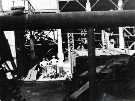 Photograph of five men in the middle distance surrounded by steel structures and large pipes, described as the Colliery Yard, Easington