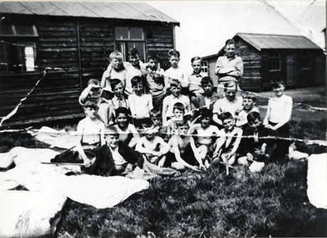 Photograph of a group of twenty two boys aged approximately twelve years, outside a wooden hut; the boys are described as being at a school camp