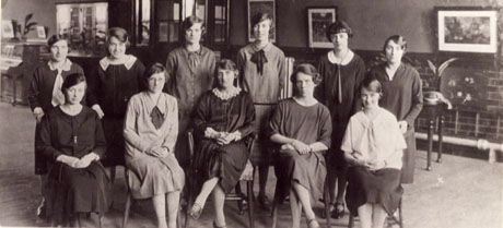 Photograph of a group of eleven female teachers in the interior of what appears to be a school hall; the teachers are described as the staff of the Junior Mixed School at Easington Colliery