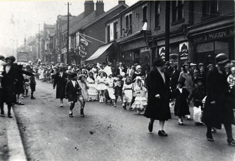 Photograph of children in fancy dress, during Easington Colliery Carnival, walking along a road, accompanied by adults, and watched by spectators ; the photograph is taken from almost the same place as easc0039, but is looking along rather than across the road