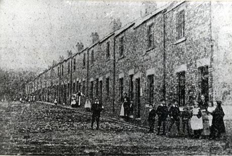 Photograph of a street of terraced houses showing the facades of the houses and a number of women and children standing near them; the image is indistinct and is described as Originally 2nd Street, Easington Colliery