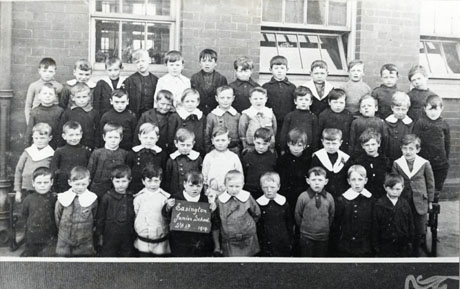 Photograph of a group of forty five boys, aged approximately five years, posed outside a brick built building; a boy on the front row is holding a notice which reads Easington Junior School Std 1B 1919
