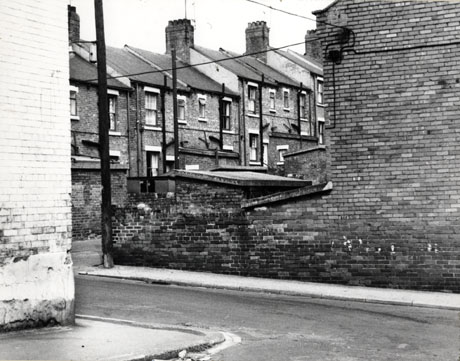 Photograph showing the exterior side wall of a terraced house and the wall of the yard of the house; beyond the wall can be seen the exteriors of the backs of terraced houses; the photograph is described as Colliery Houses, Easington Colliery, 1976