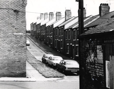 Photograph of one side of a street of terraced houses rising up a steep hill; the photograph is taken from Alnwick Street and shows 14th Street North; four cars are parked in 14th Street North