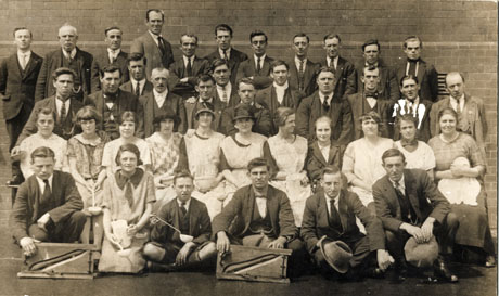 Photograph of the staff of twenty seven men, eleven women, one boy and one girl of a soup kitchen, posed against a wall in the yard of the Senior Girls' School, Easington Colliery; the women are holding jugs, basins and ladles and the men cutting devices