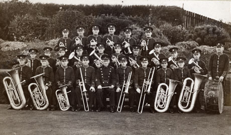 Photograph of members of the Easington Colliery Welfare Band posed with their instruments in front of a bank of flowers; the members are wearing uniform